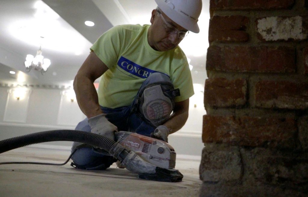 A Concreate worker using a hand grinder on a concrete surface.