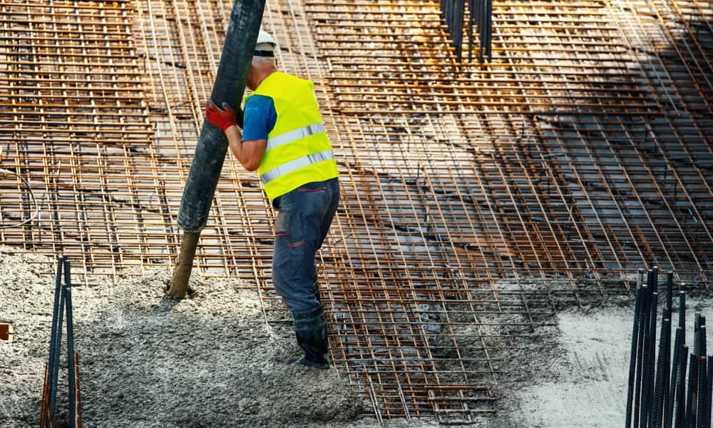 A construction worker pouring concrete over rebar mesh. 