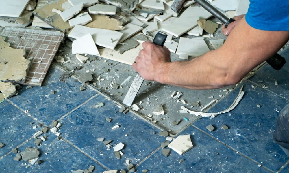 A tile specialist removing tiles with a chisel and hammer.